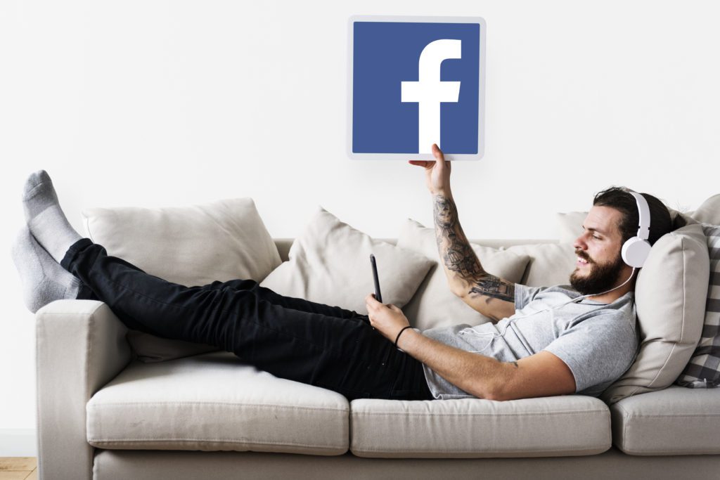 Caucasian man enjoying music at home holding a play button Man showing a Facebook icon
